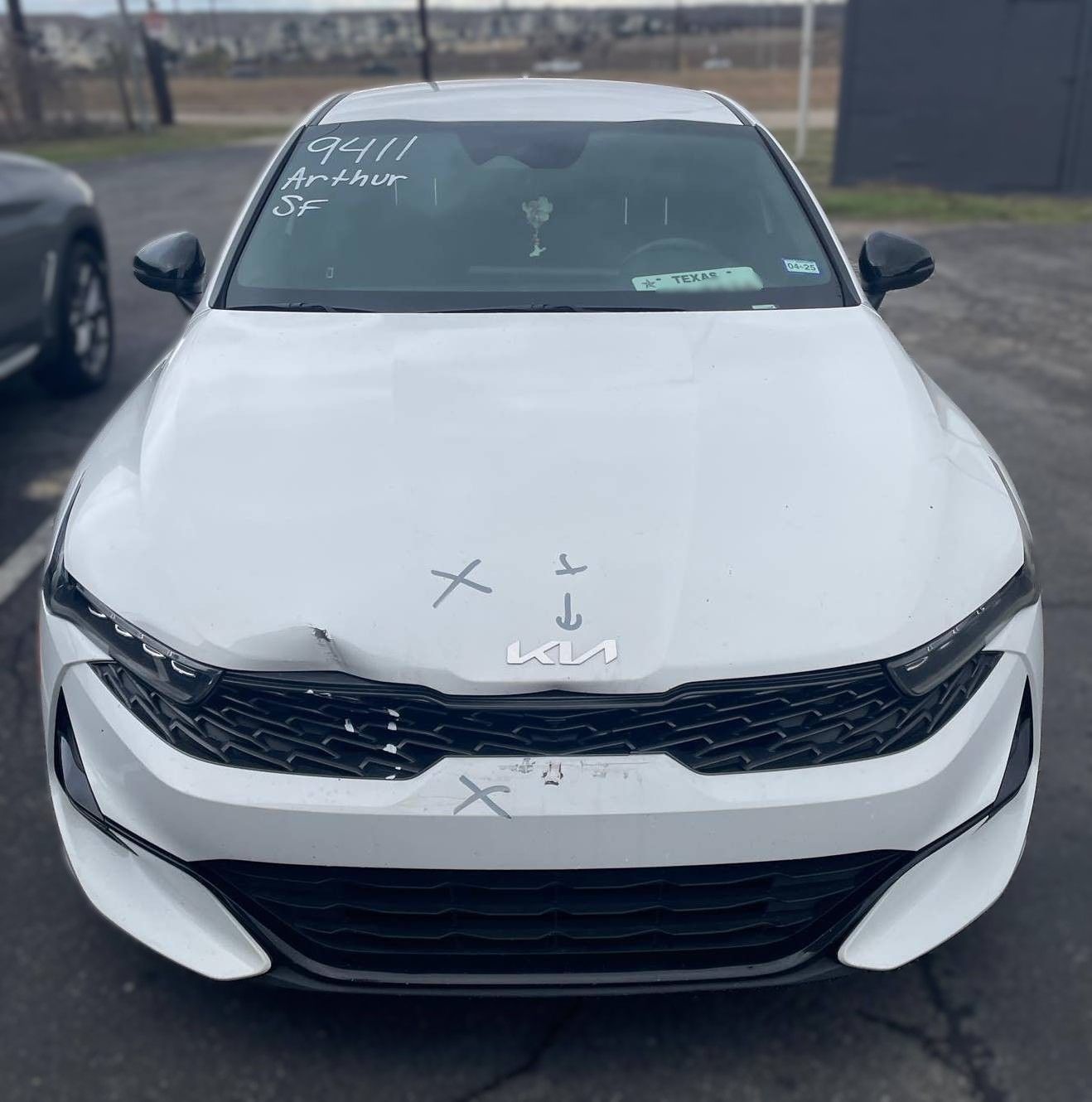 White Kia sedan with front-end damage, marked with Xs.