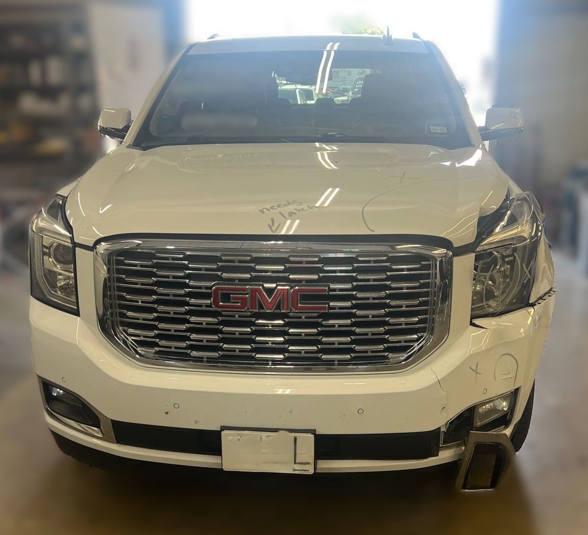 White GMC Yukon SUV with damage to the front bumper and hood, parked outdoors.