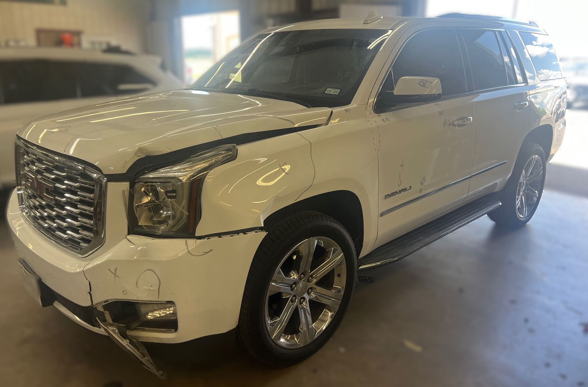 White GMC Yukon SUV with front-end damage, parked indoors.