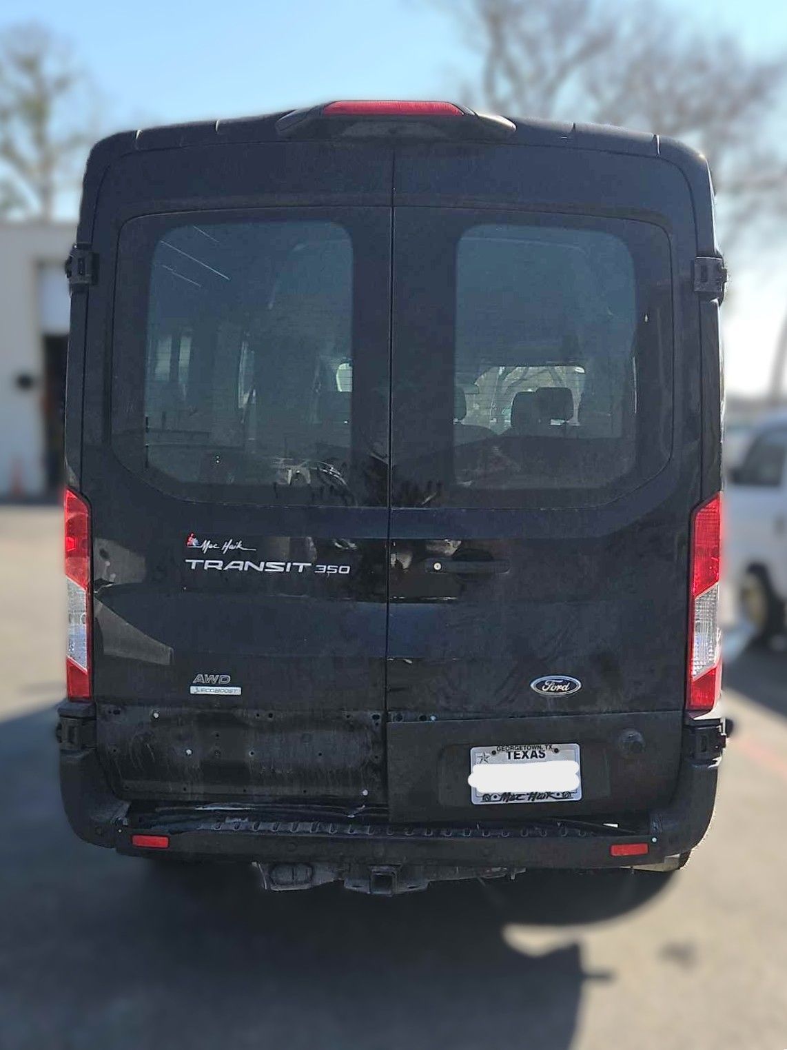 Black Ford Transit van from the rear, parked outside on a sunny day.