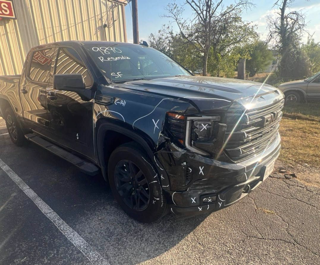 Black GMC pickup truck with front-end damage parked near a building. White markings are on the vehicle.