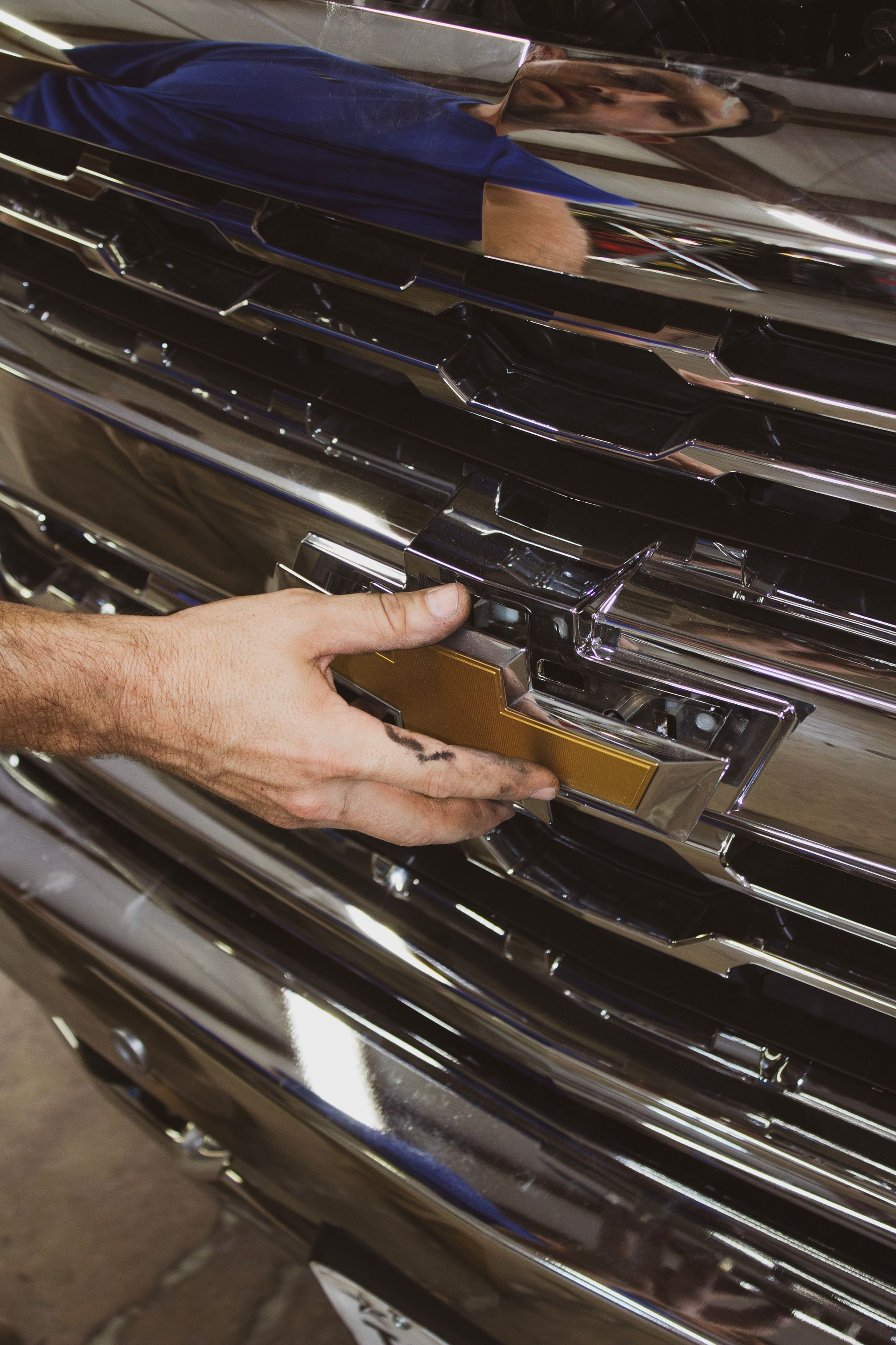 Hand touching the gold Chevrolet emblem on a chrome grill.