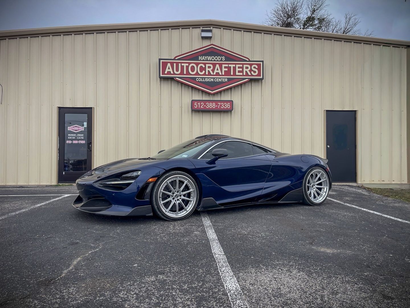 Blue McLaren 720S sports car parked in front of Autocrafters shop.