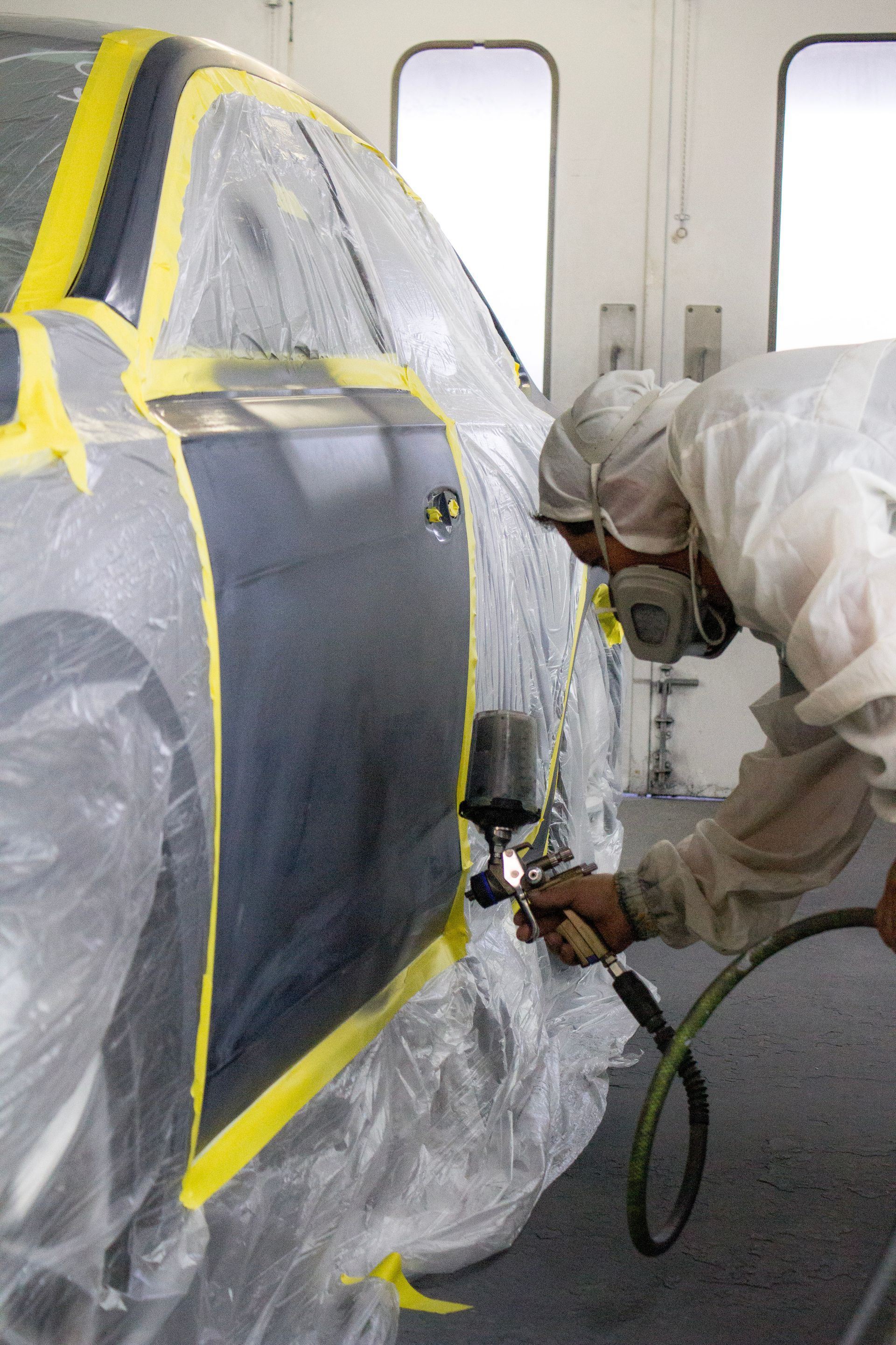 Person in protective suit spraying a car door with a paint gun in a paint booth.