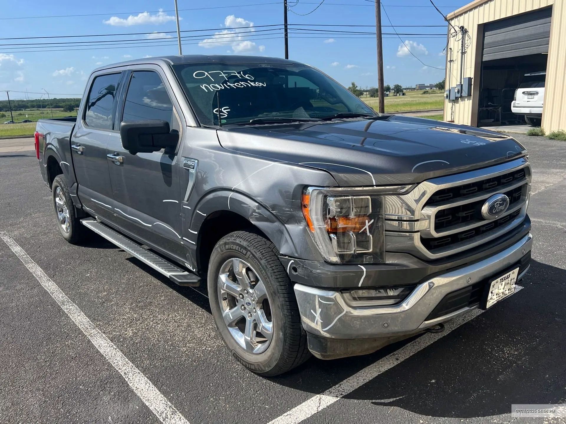 Gray Ford F-150 pickup truck with damage to the front is parked outside a building on a sunny day.
