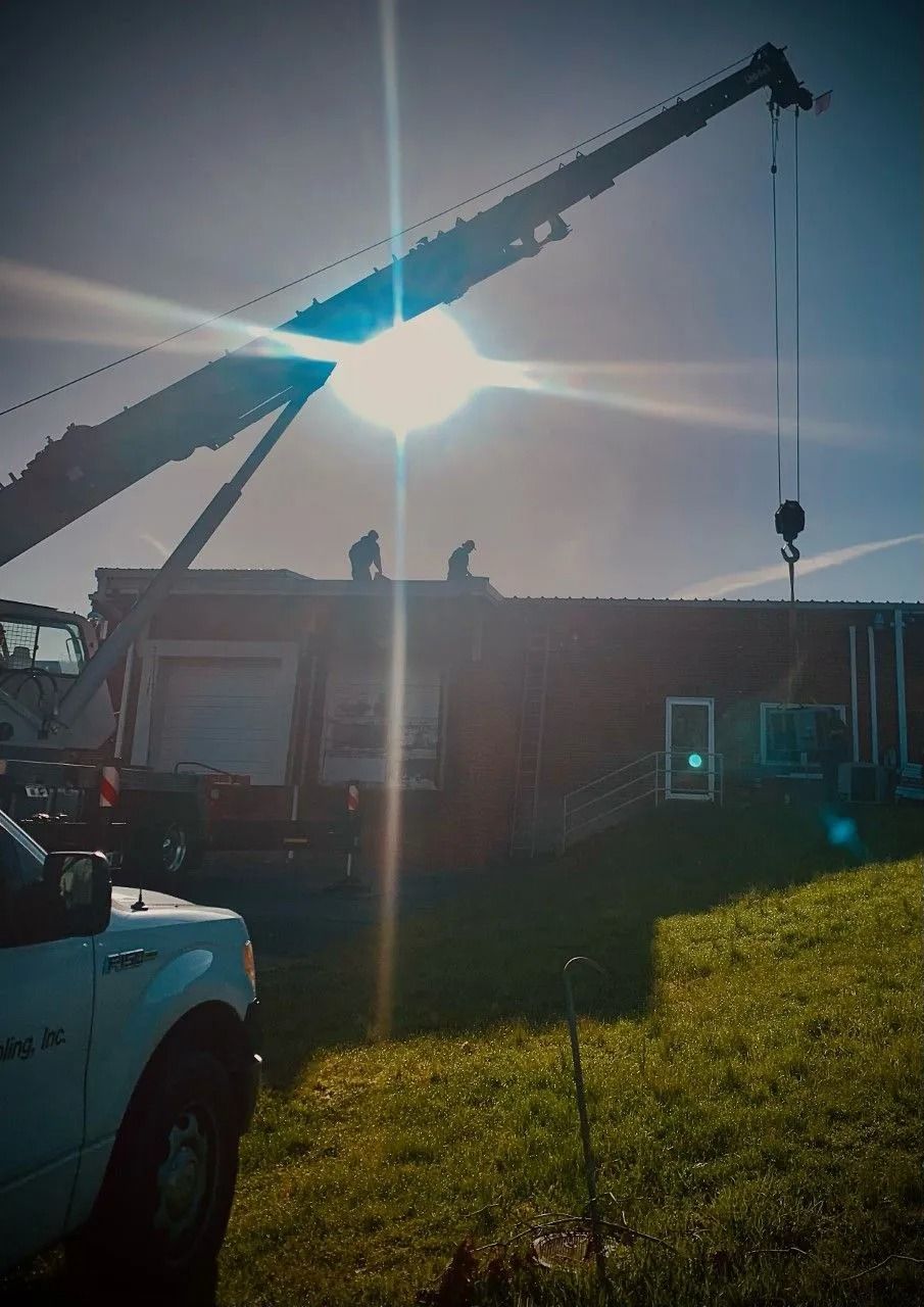 Crane lifting a building's roof; workers on top. Bright sunlight obscures the sky and foreground.