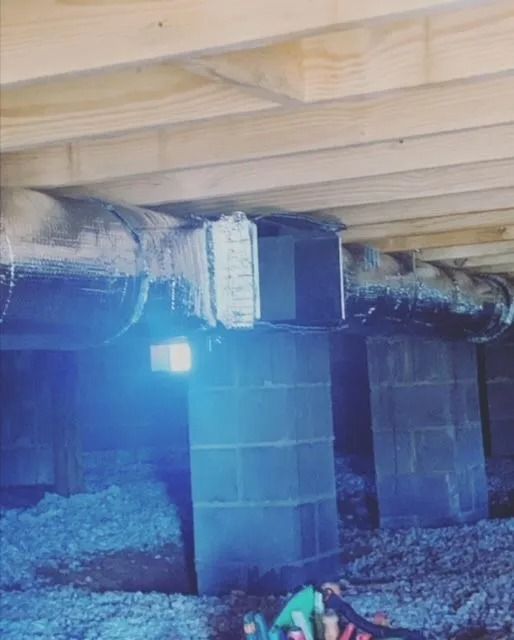 Underneath a house: cinder block supports, insulation, ductwork, and wooden beams.