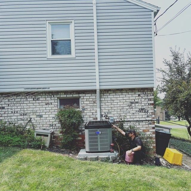 Person inspecting air conditioner unit near a house, outside.