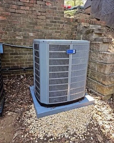 Air conditioning unit, gray and blue, on a concrete pad, near a brick wall and gravel.