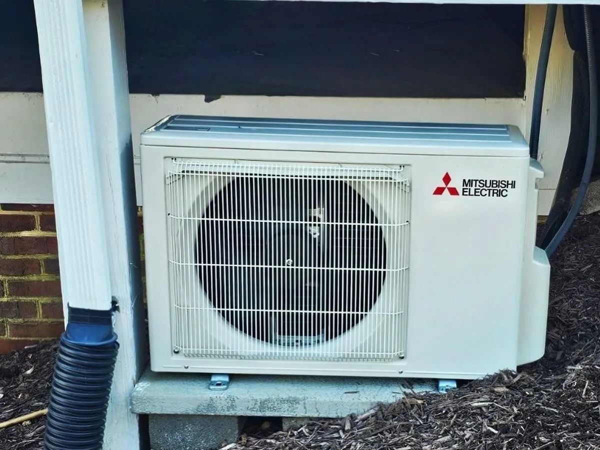 White Mitsubishi Electric heat pump next to a downspout, mounted near a building's exterior.