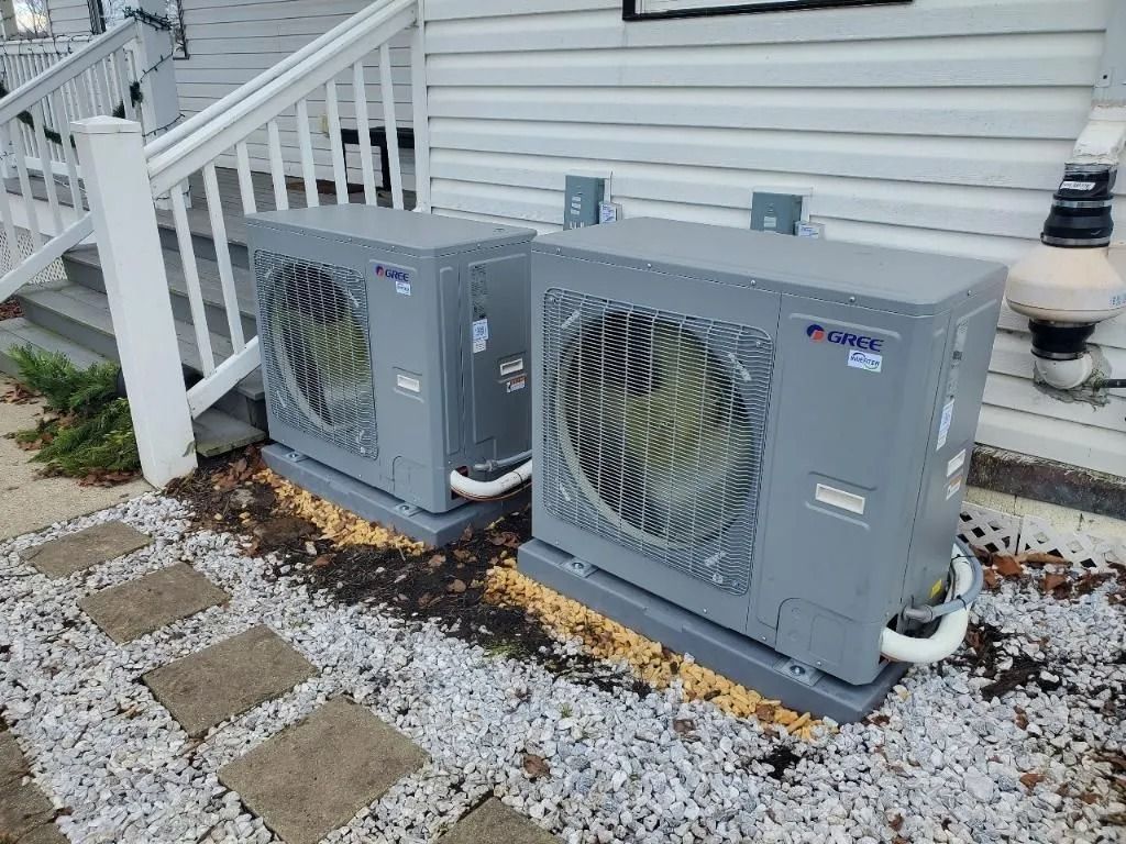 Two gray Gree heat pump units outside a white building next to stone pavers and stairs.