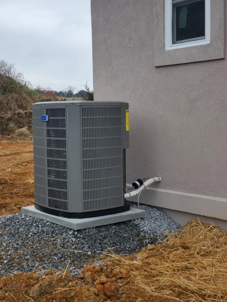 AC unit on a concrete pad next to a building, on a bed of gravel and dirt, on an overcast day.