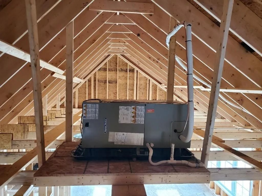HVAC unit installed in an unfinished attic. Brown wooden beams support the unit on a plywood platform.