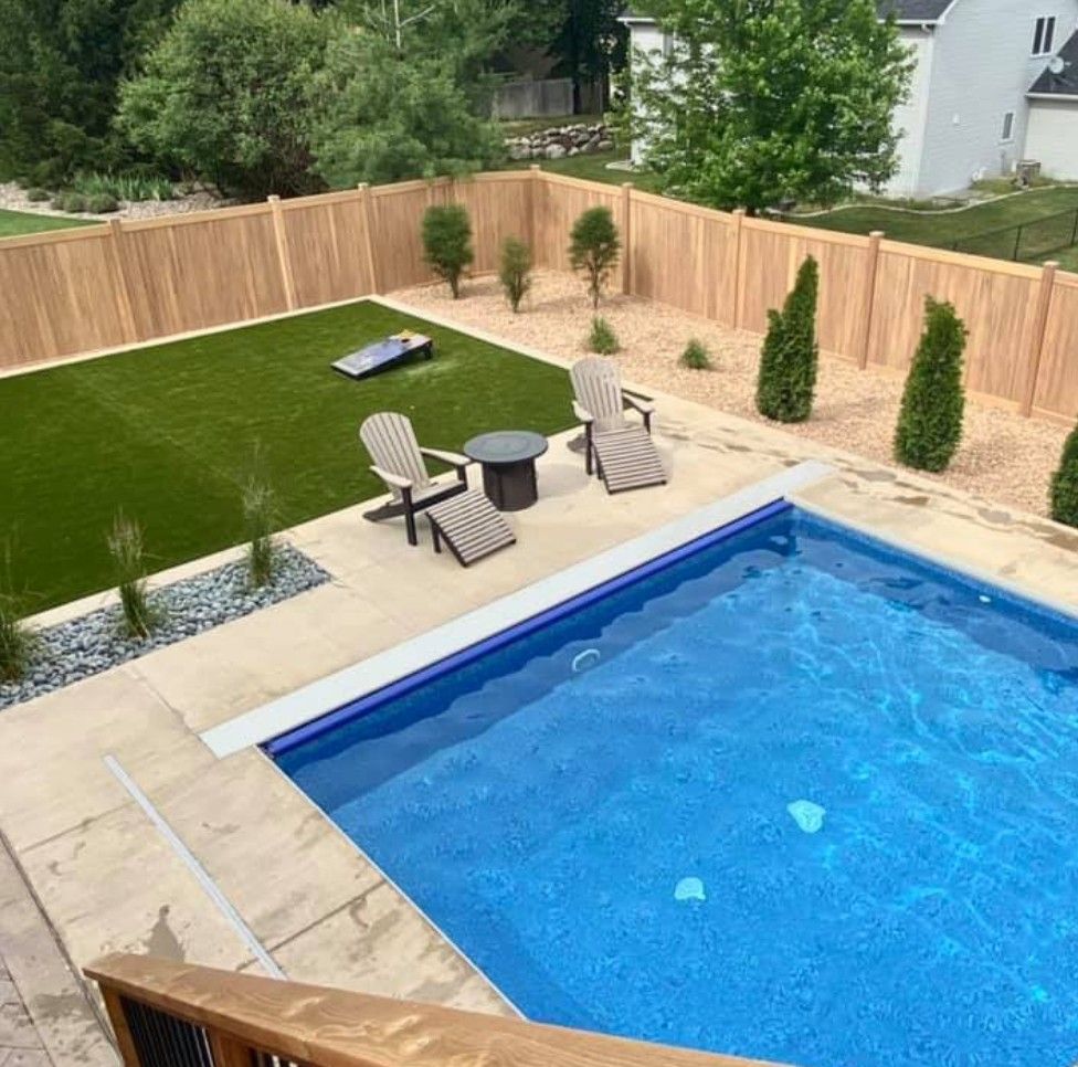 Backyard with pool, artificial lawn, wooden fence, lounge chairs, and bean bag toss game.
