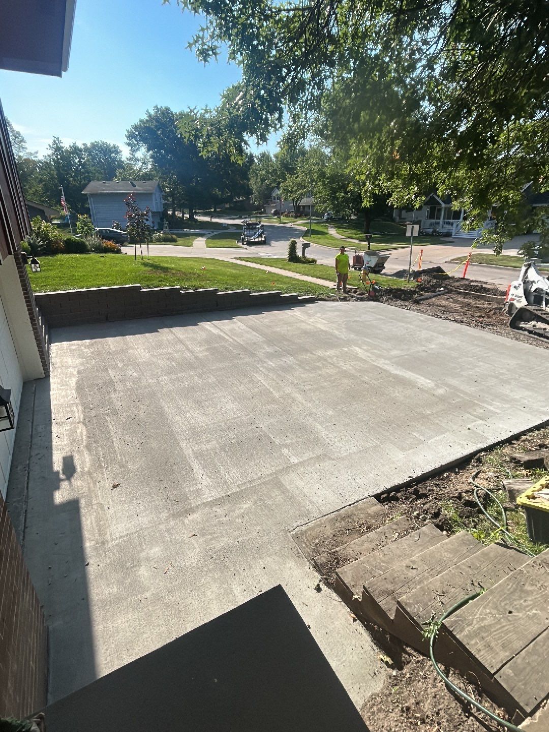 Newly poured concrete driveway with workers, house, and green yard in the background.