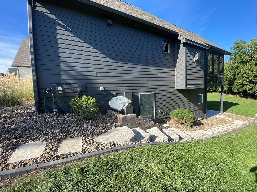 Black house exterior with steps leading to a door and landscaping with small plants and a grassy yard.