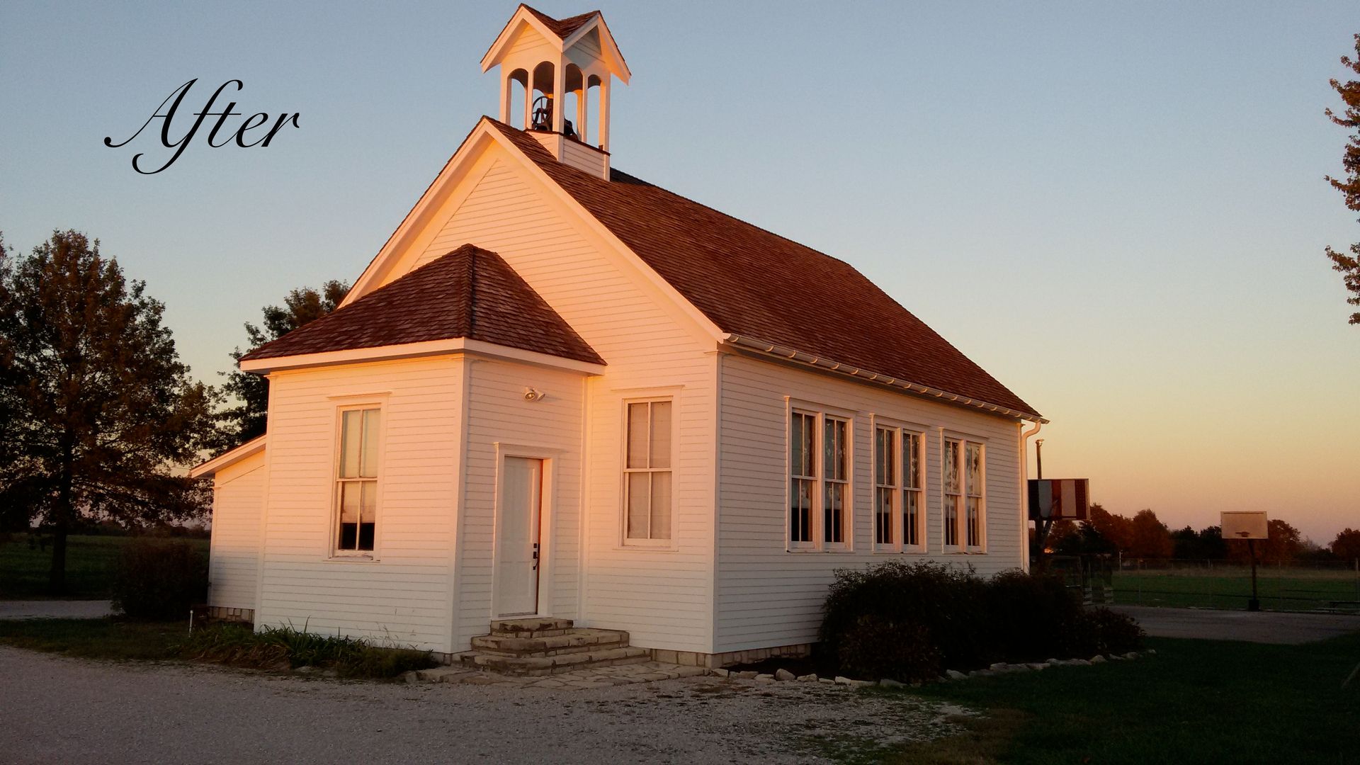 Small white church at sunset with a red roof and bell tower, viewed from the side.