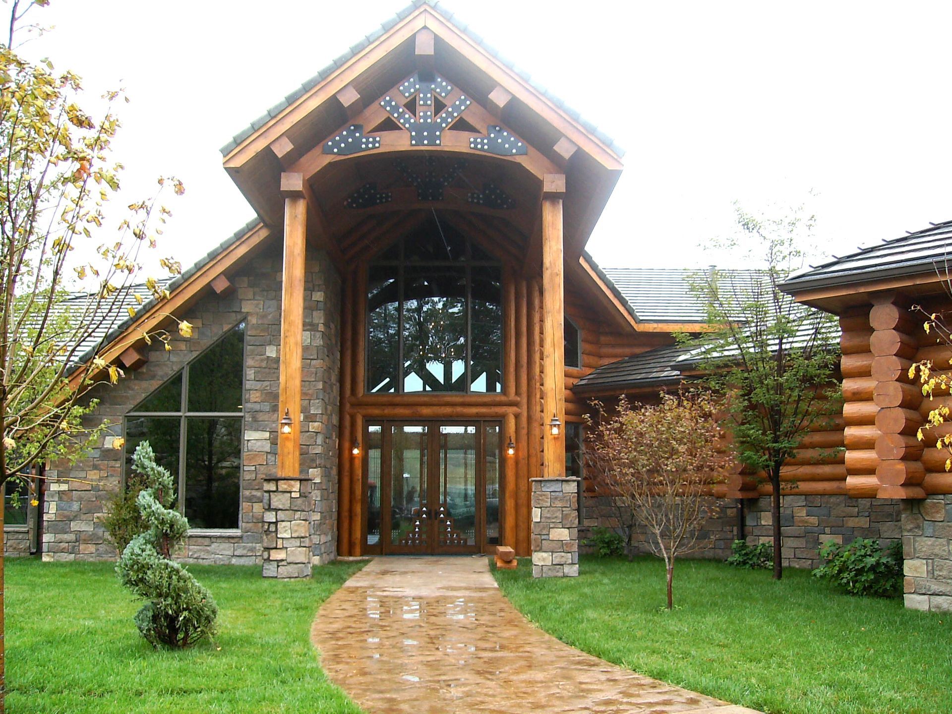 Rustic lodge entrance with stone walls, wood beams, and a curved brick path through green lawn