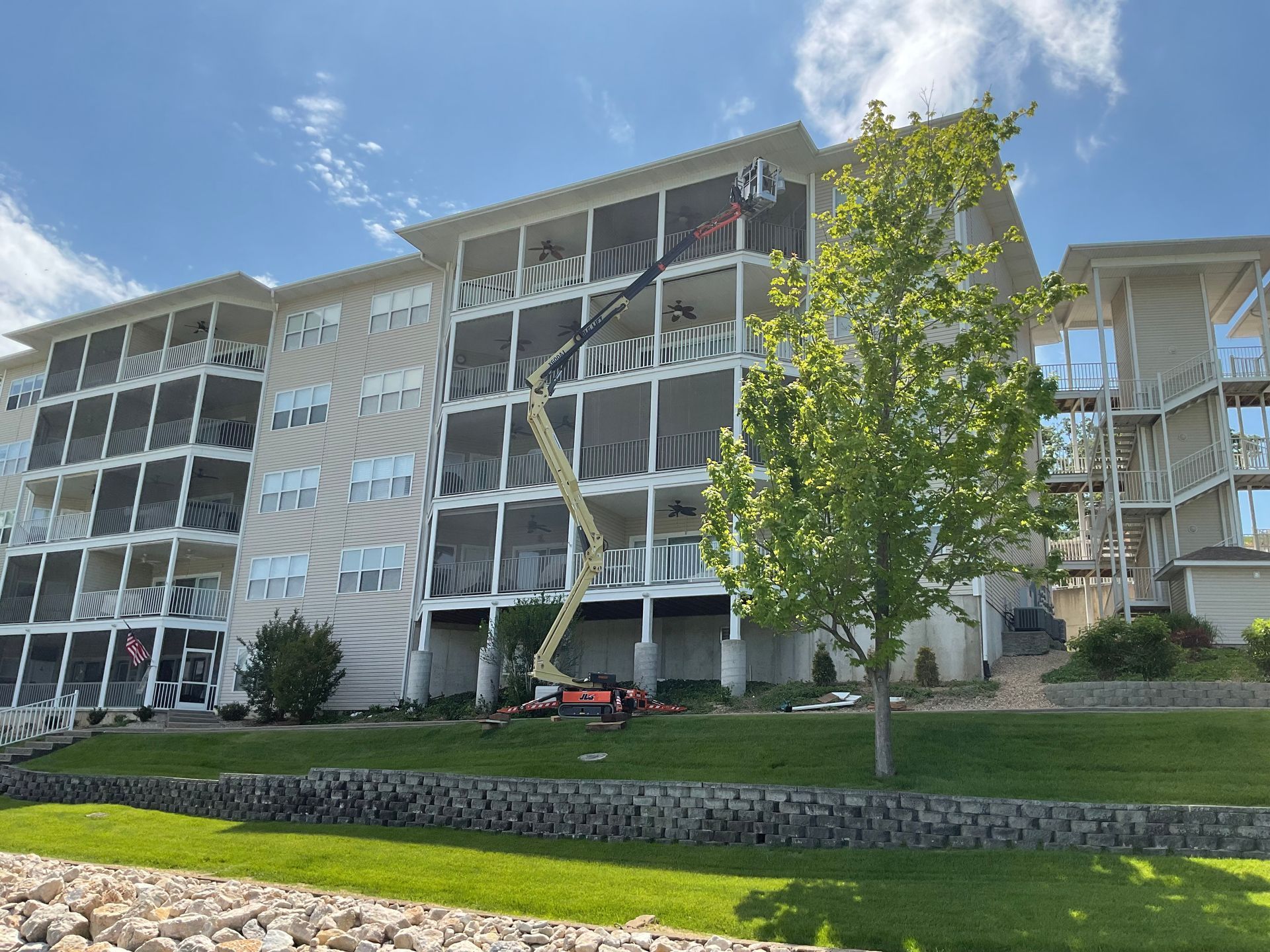 Apartment buildings with balconies behind a grassy lawn and a tree on a sunny day