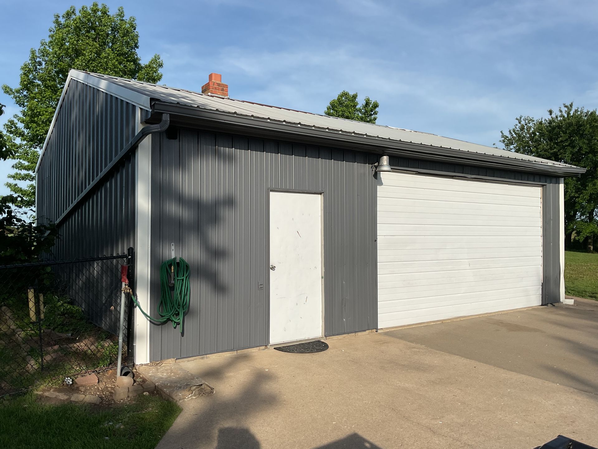 Gray metal garage with white doors and a concrete driveway, viewed from the front in daylight