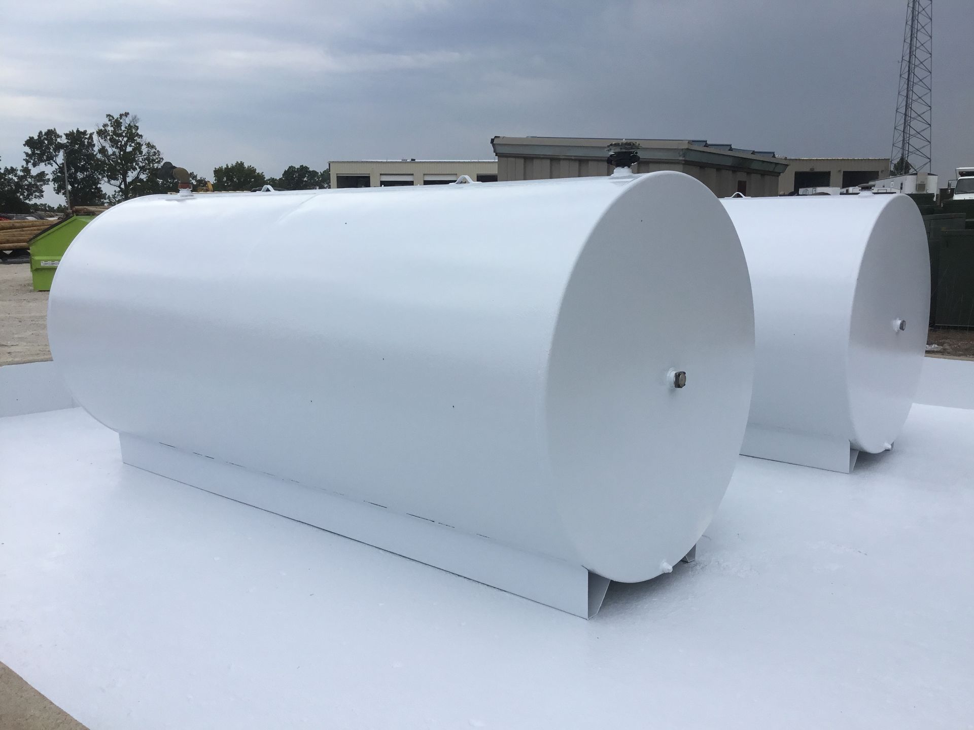 White cylindrical tanks on a paved lot outdoors under an overcast sky