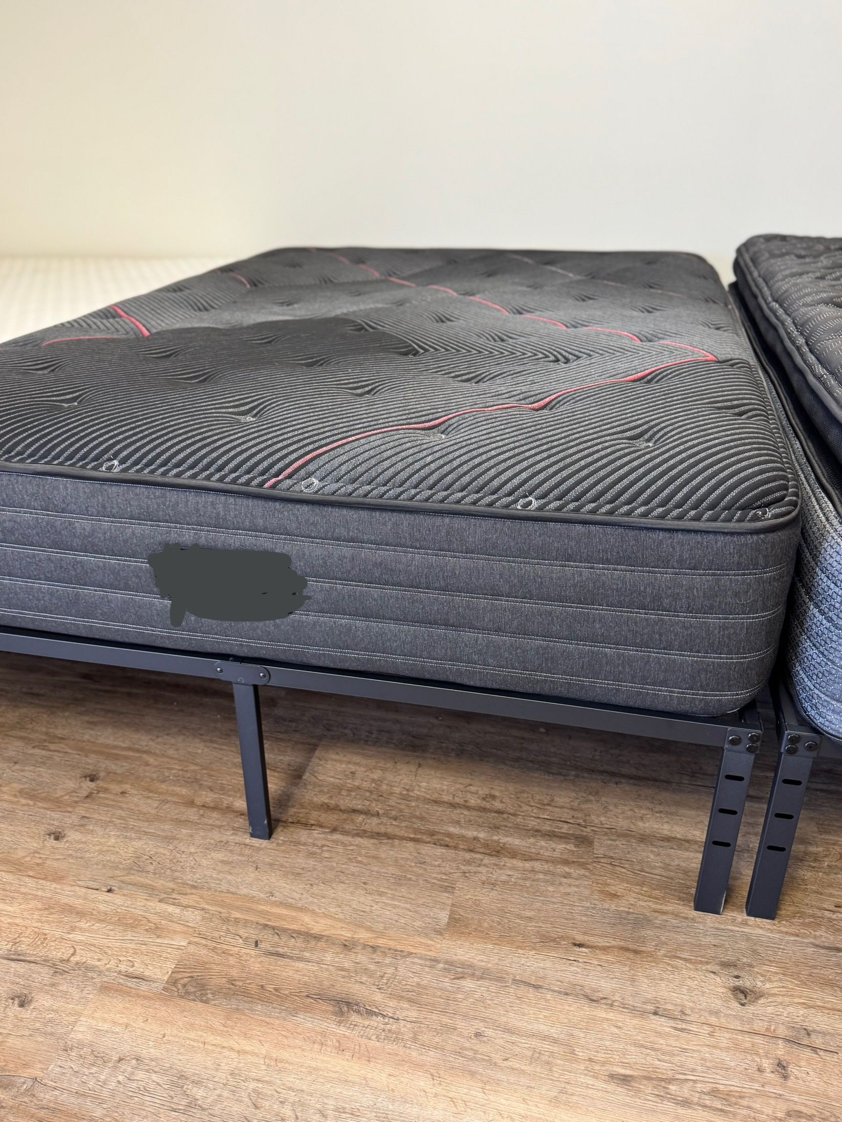 Black mattress on a metal bed frame in a sparsely furnished room with wooden floor.