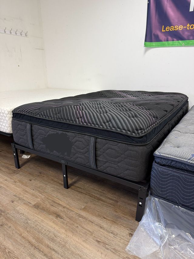 Black mattress on a metal bed frame in a room with wood floor and a second bed nearby