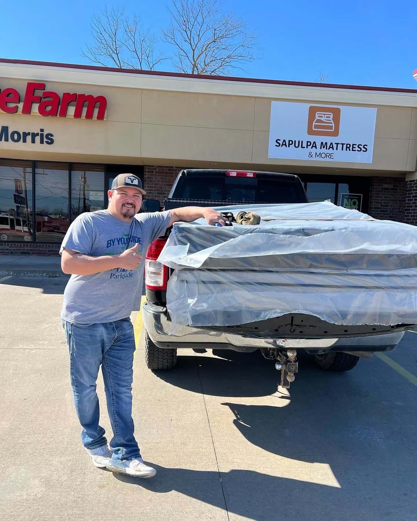 Man standing beside a truck loaded with wrapped mattresses in front of a mattress store