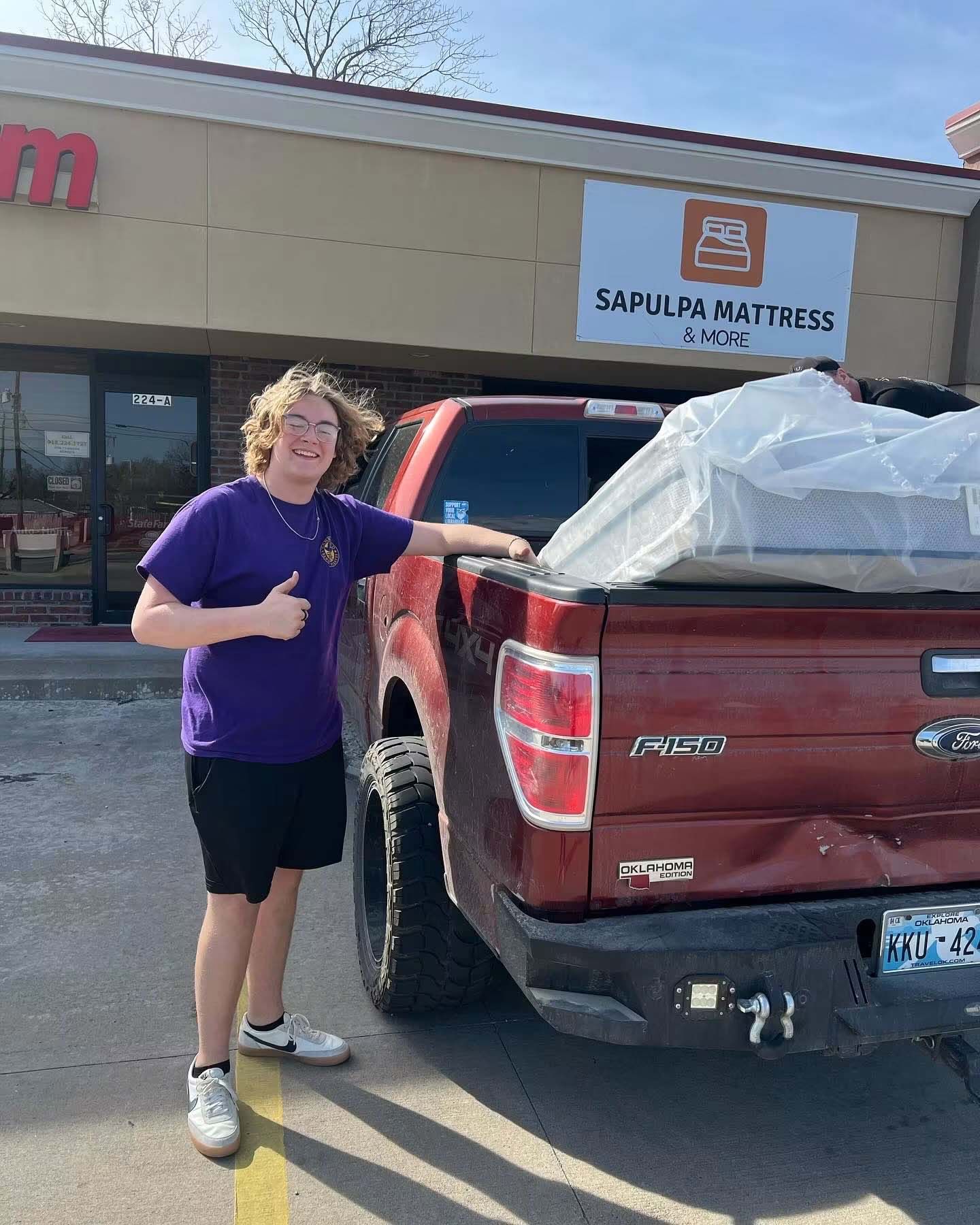 Person standing beside a red pickup truck outside a store, giving a thumbs-up.