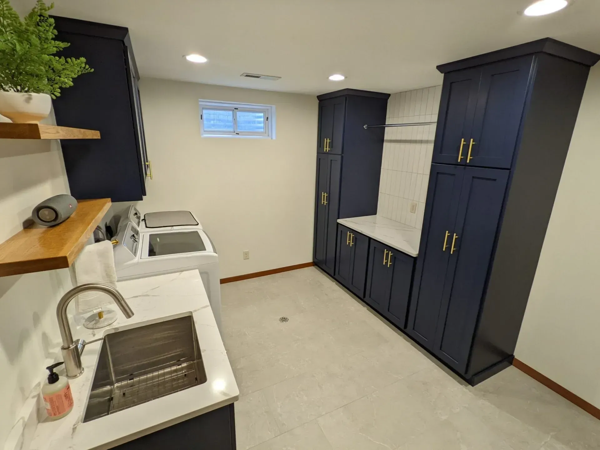 A laundry room with blue cabinets , a sink , a washer and dryer , and a window.