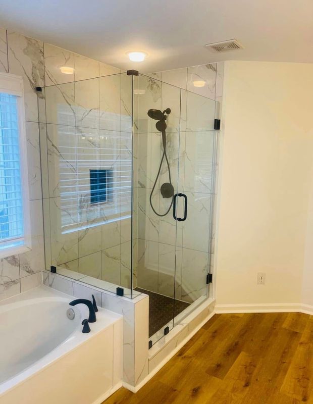 Bathroom with glass shower, white tub, and warm wood flooring in a bright corner room