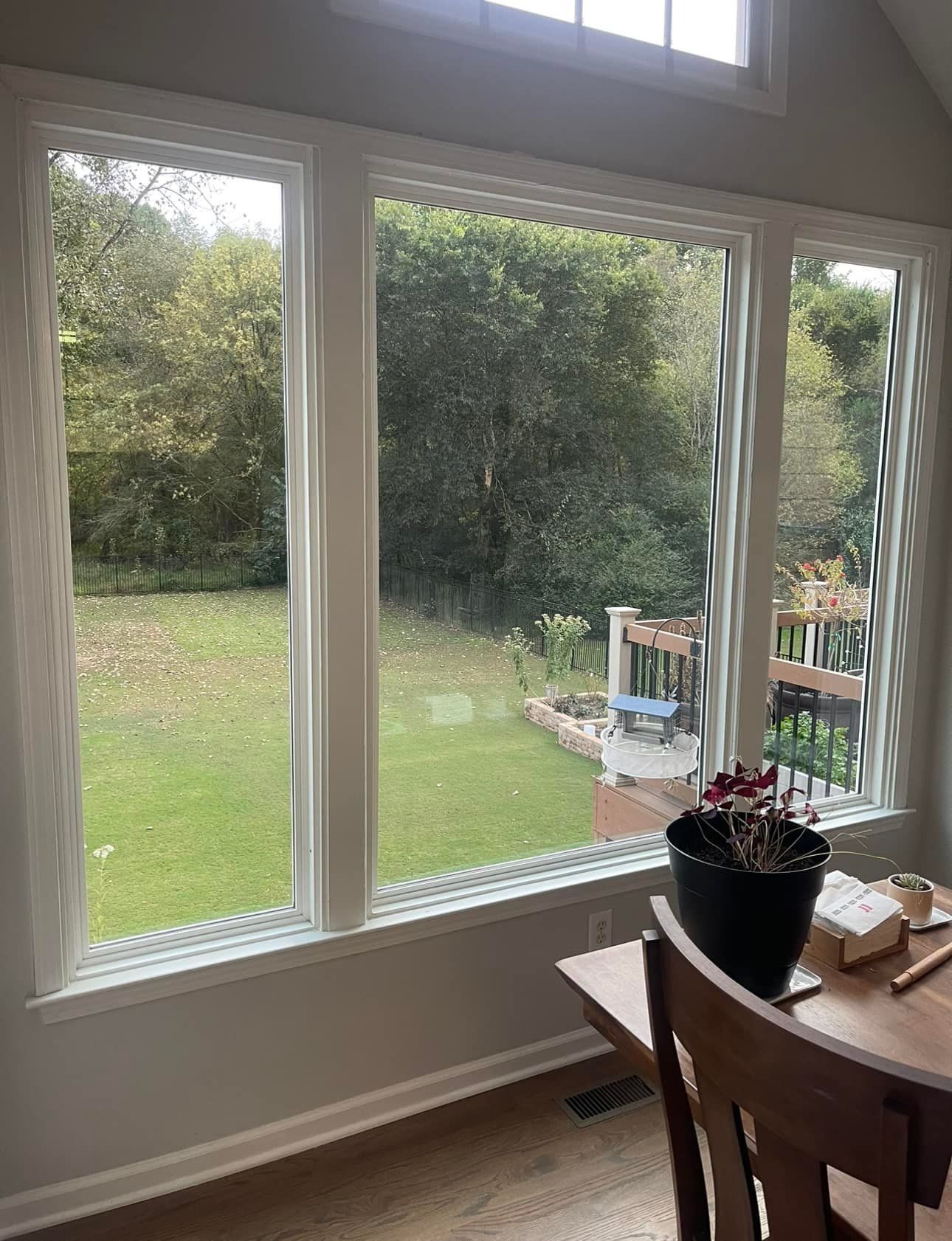 Dining area with large windows overlooking a green backyard and wooden deck.
