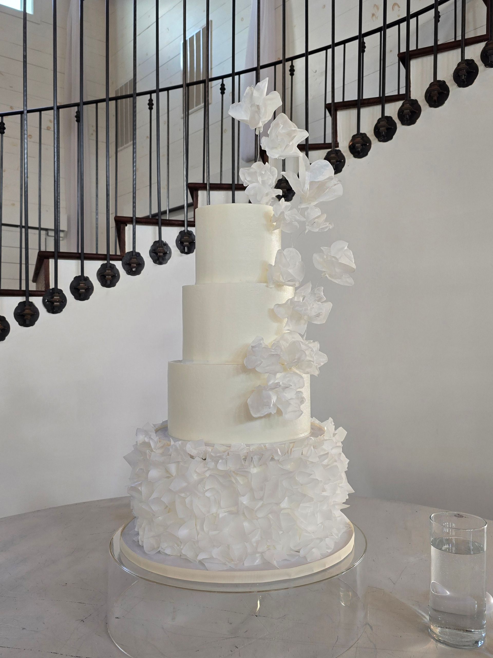A white wedding cake is sitting on a table in front of a staircase.