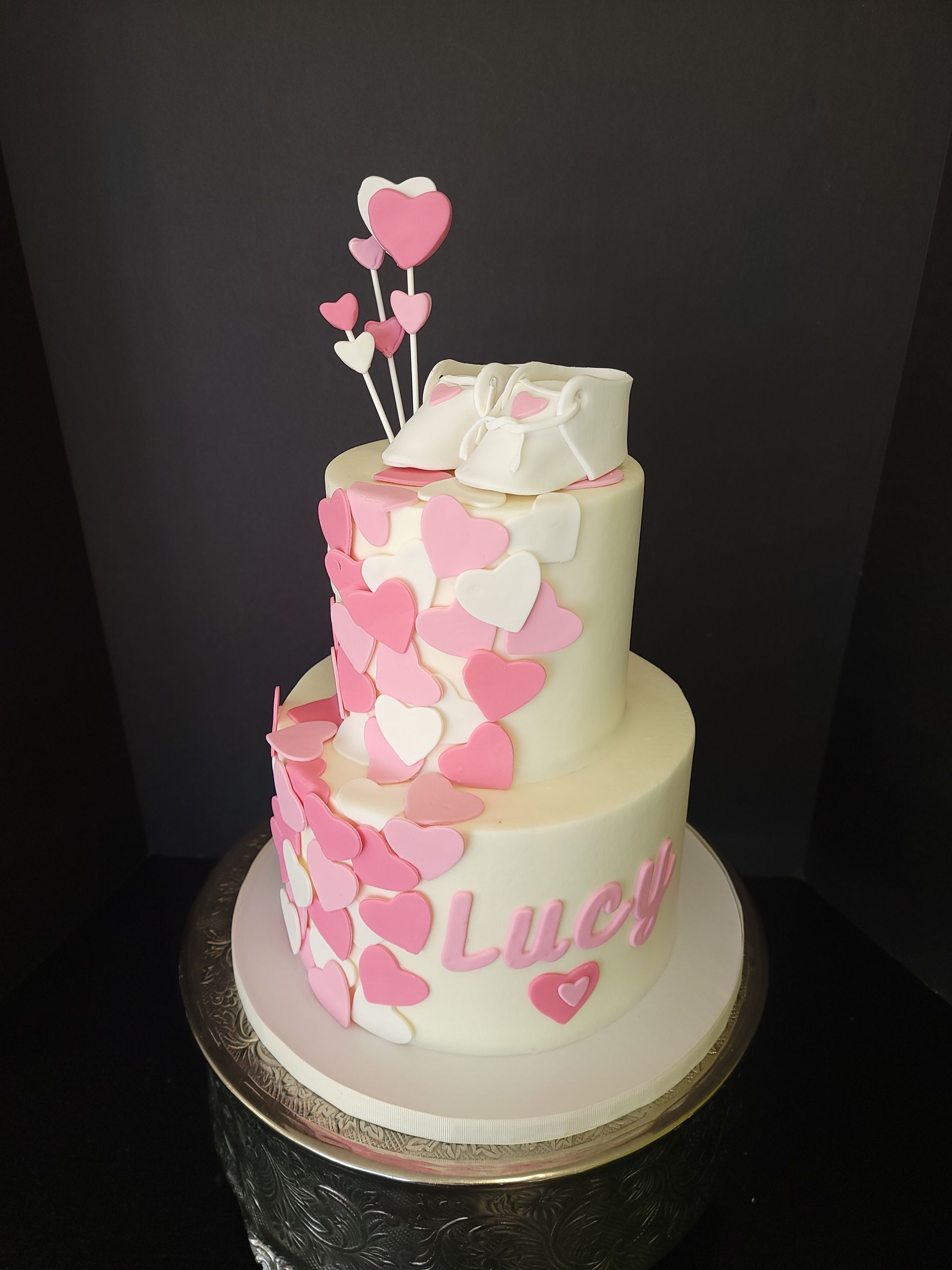 A white cake with pink hearts and the name Lucy on it