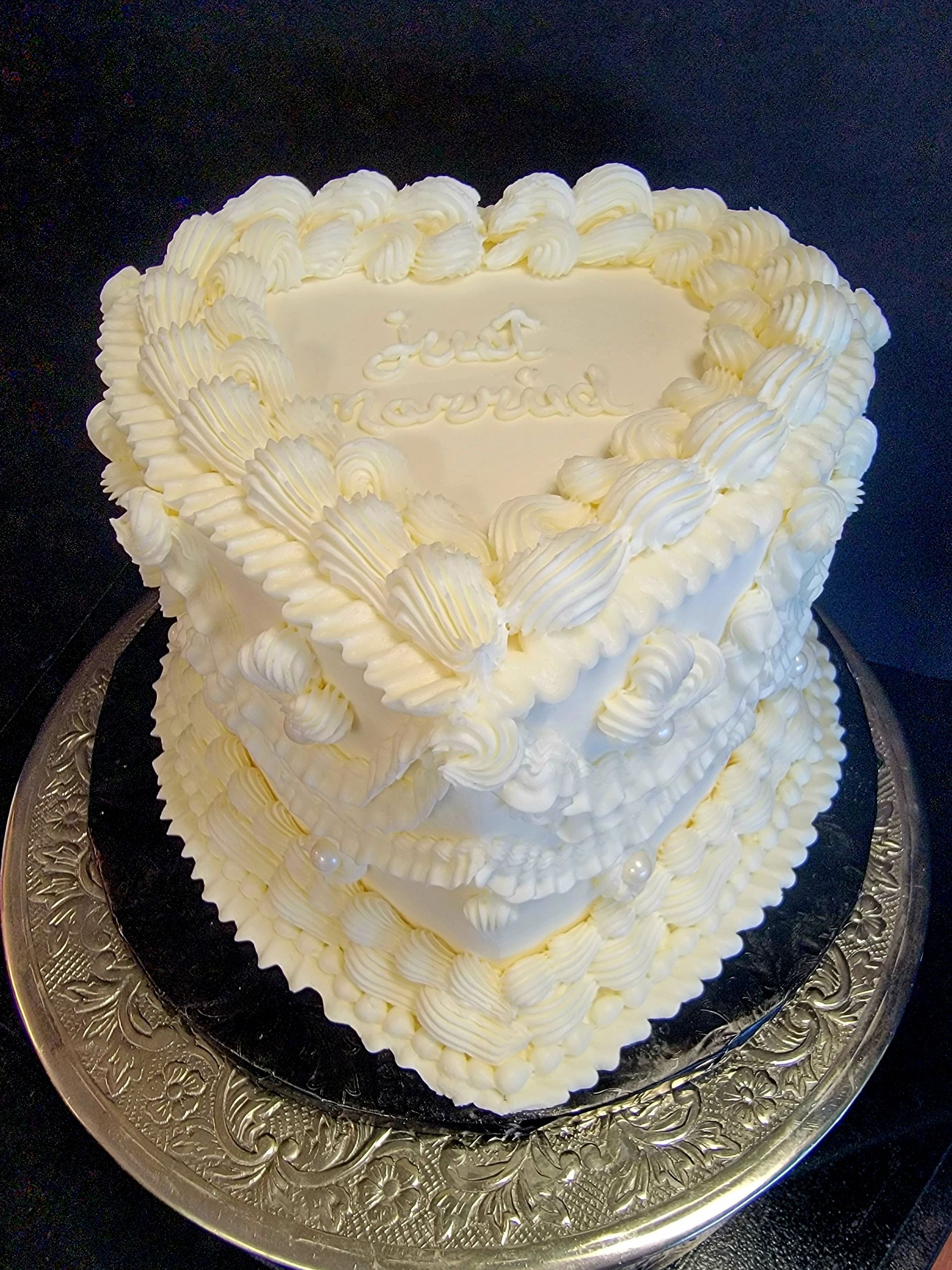 A heart shaped cake with white frosting is sitting on a silver plate.
