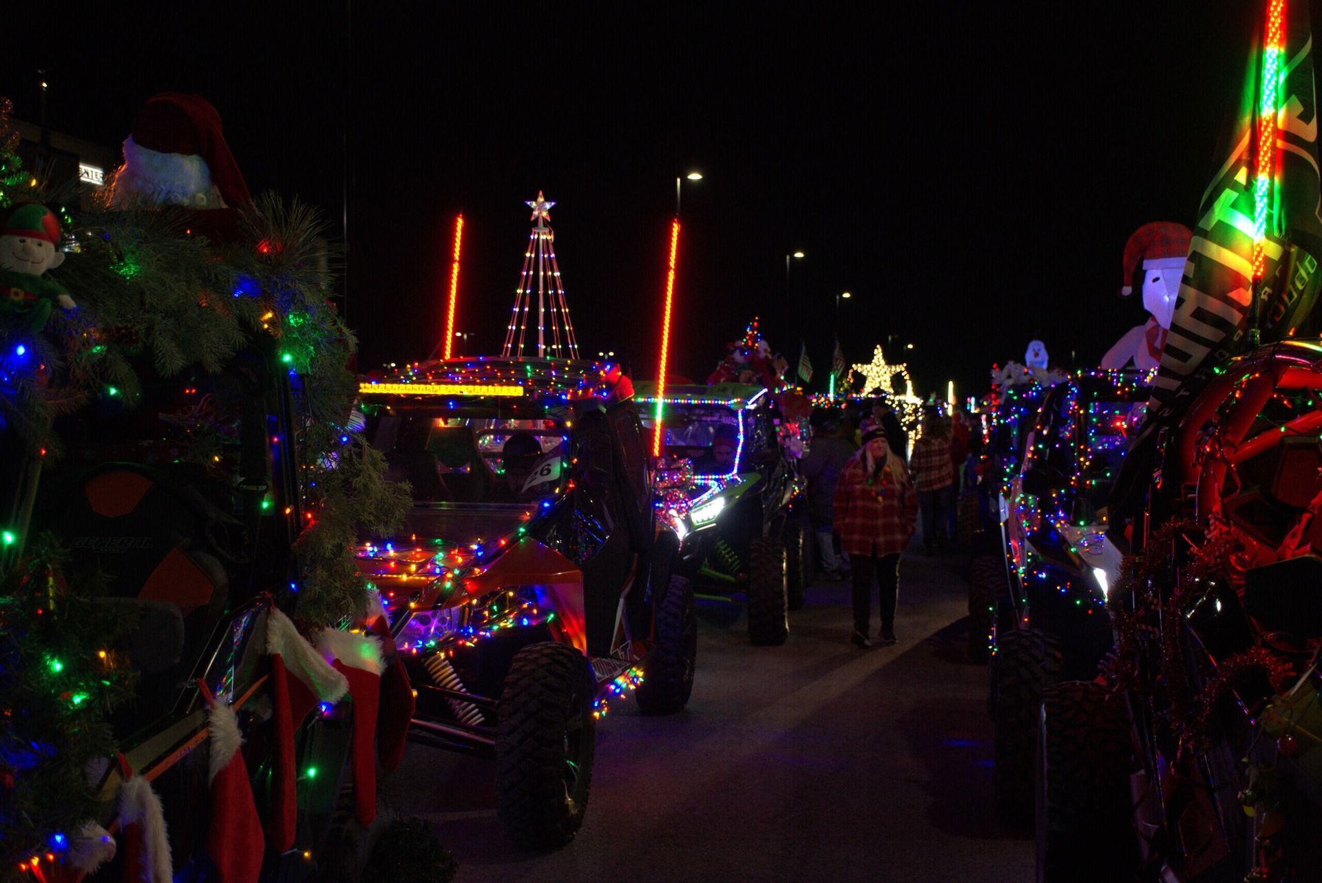 Off-road vehicles decorated with colorful holiday lights participate in an evening Christmas parade.