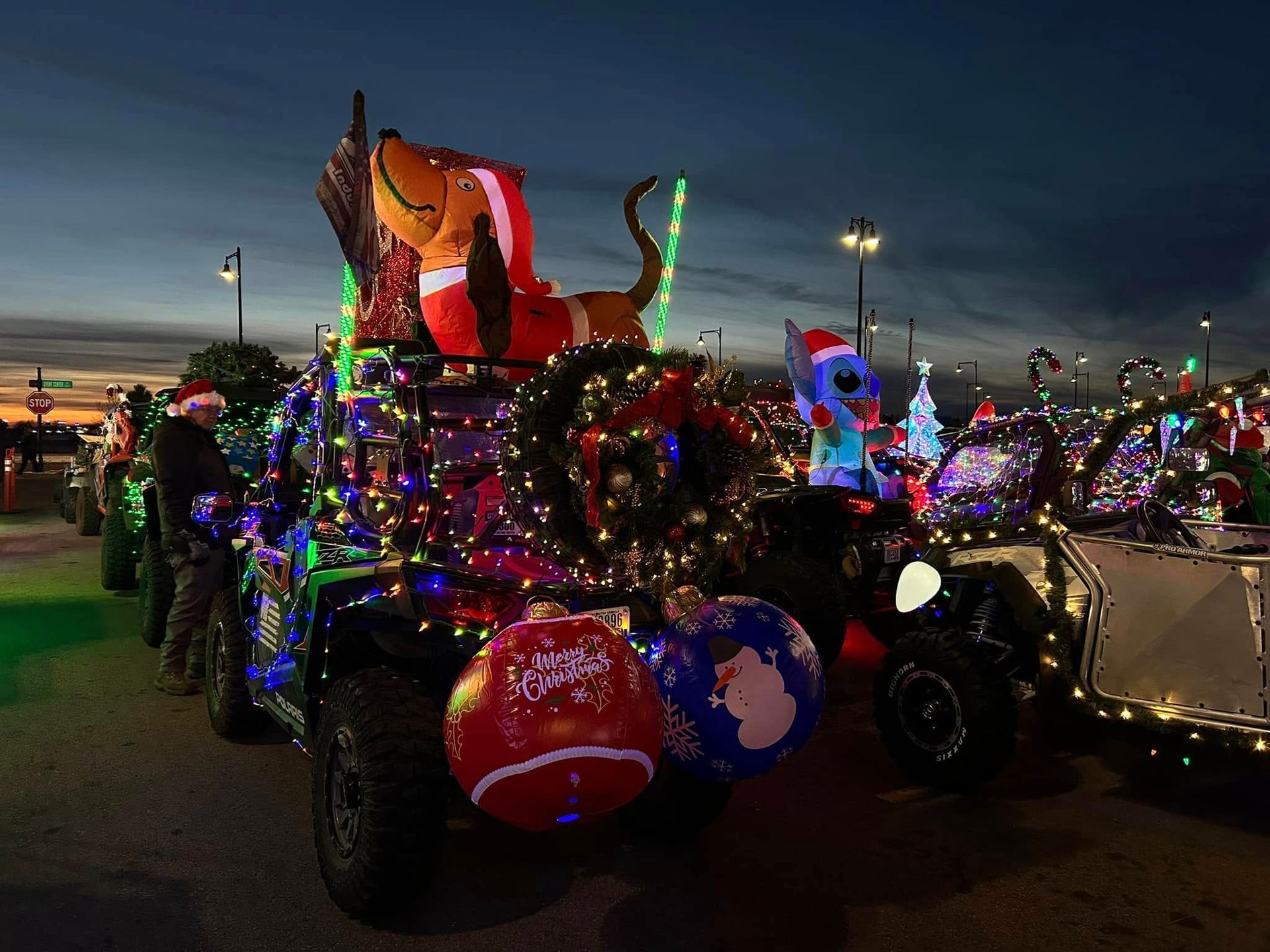 Golf carts decorated with Christmas lights, giant inflatable characters, and ornaments lined up at twilight.
