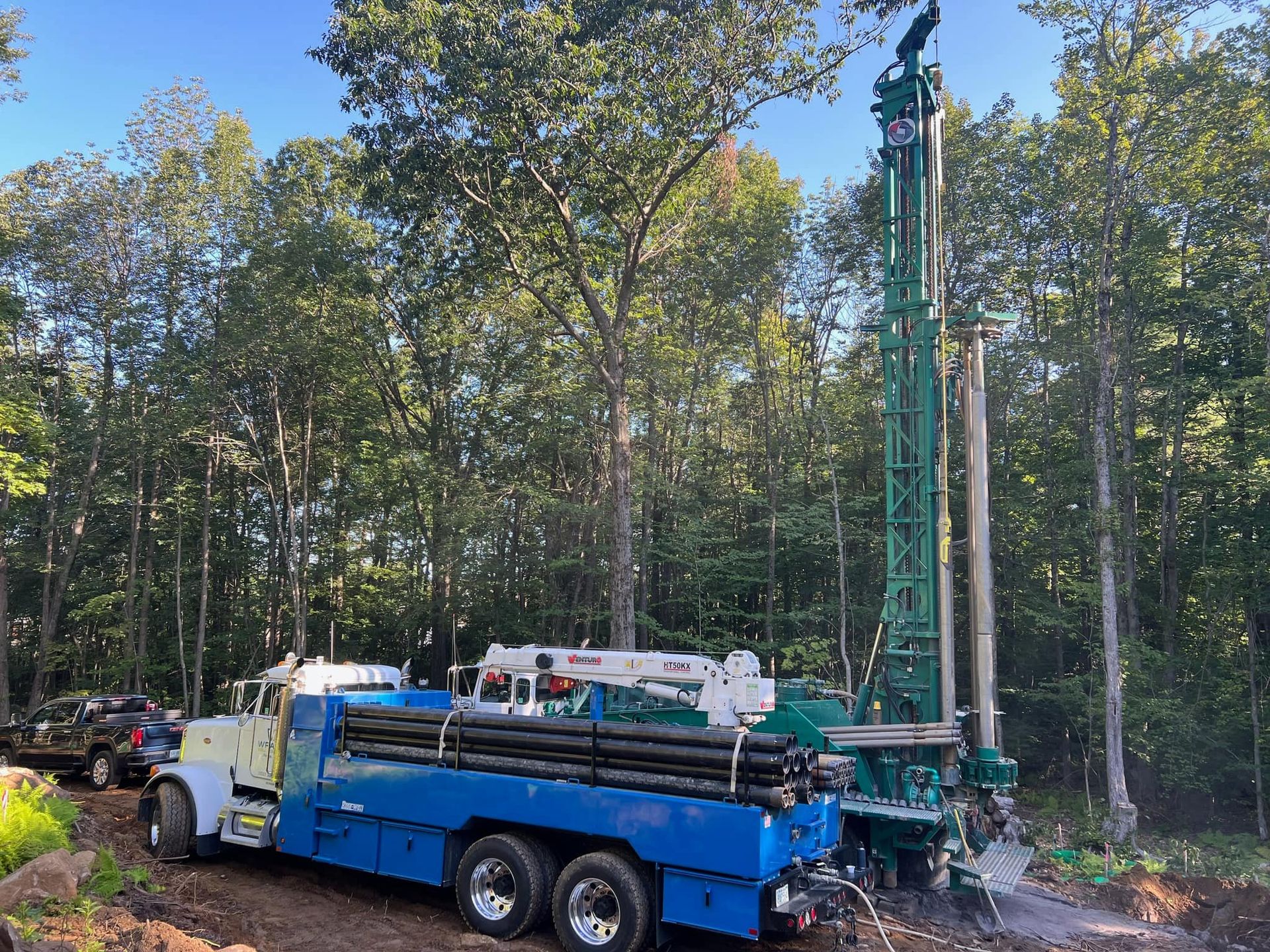 A blue truck is driving down a dirt road next to a forest.