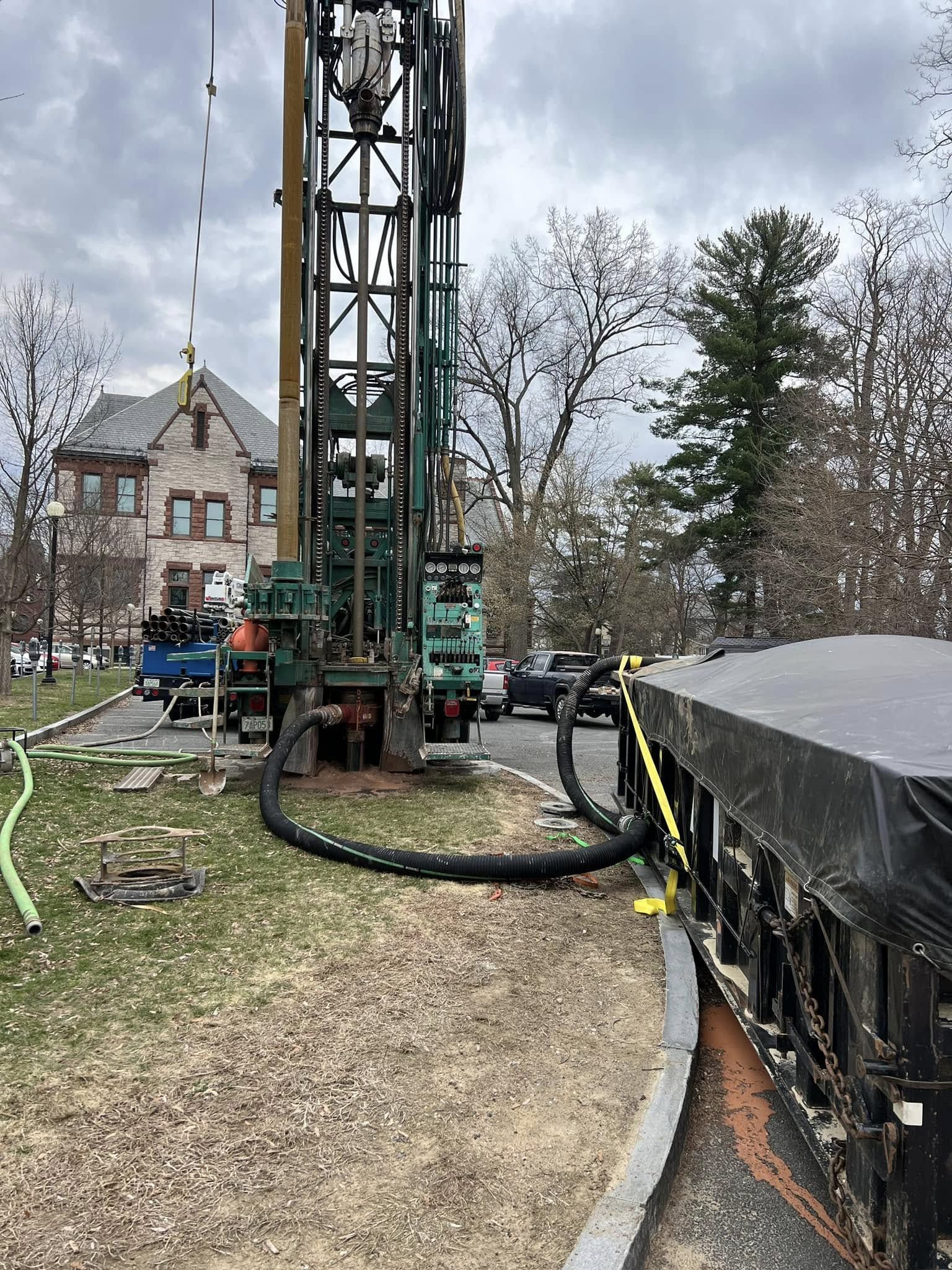 A water well is being drilled in a park in front of a building.