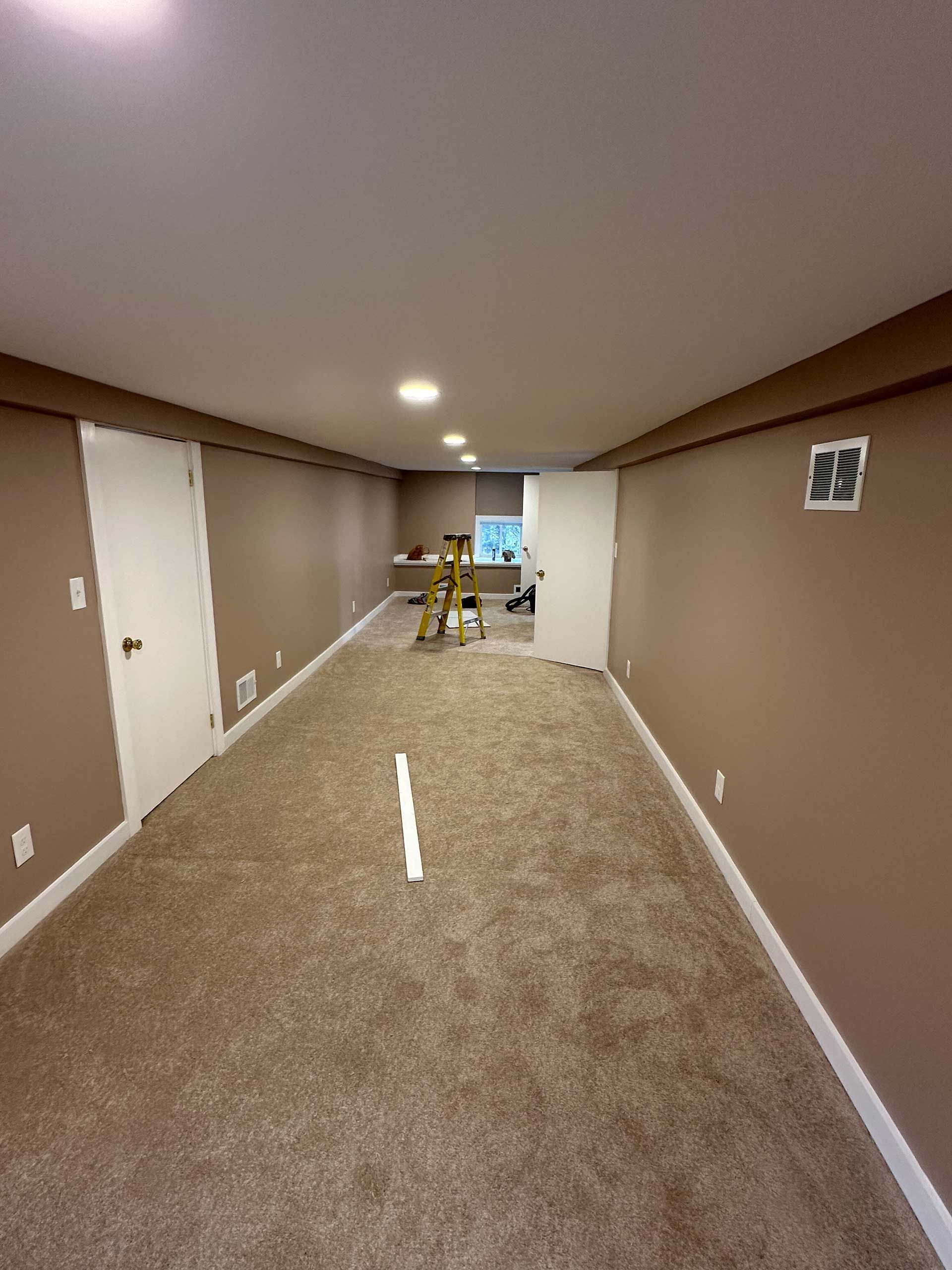 long, narrow room with tan walls and carpet, white door, trim, and ceiling
