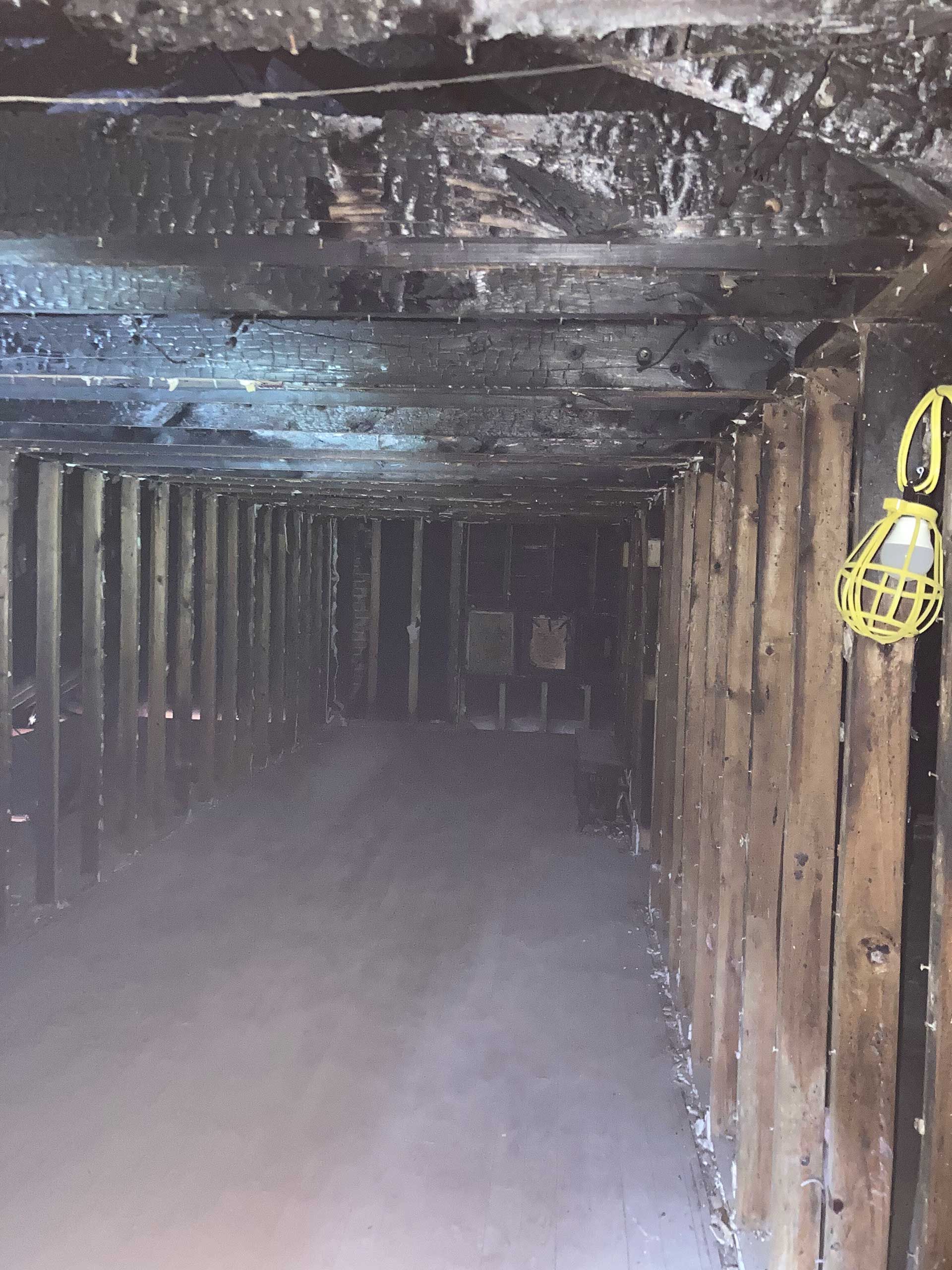 smoke-filled, charred wooden interior, light fixture hangs on the right wall; long rectangular space
