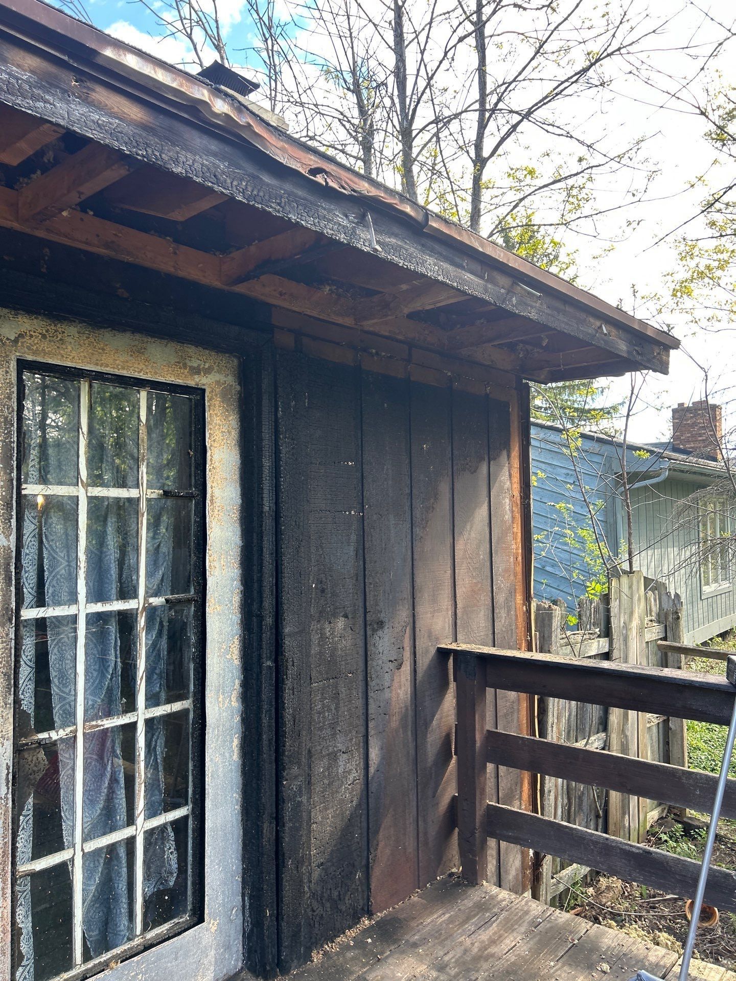 Weathered wooden cabin porch with a white-framed door and railing beside leafless trees.