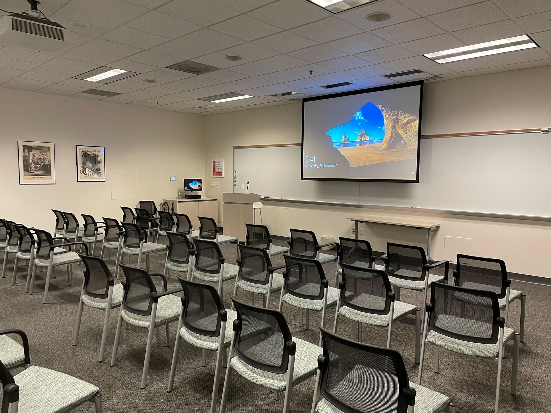 A classroom with rows of chairs and a projector screen.