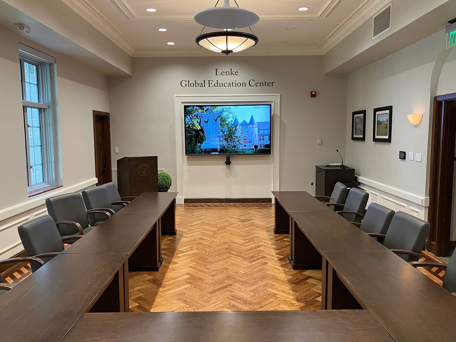 A conference room with long tables and chairs and a flat screen tv on the wall.