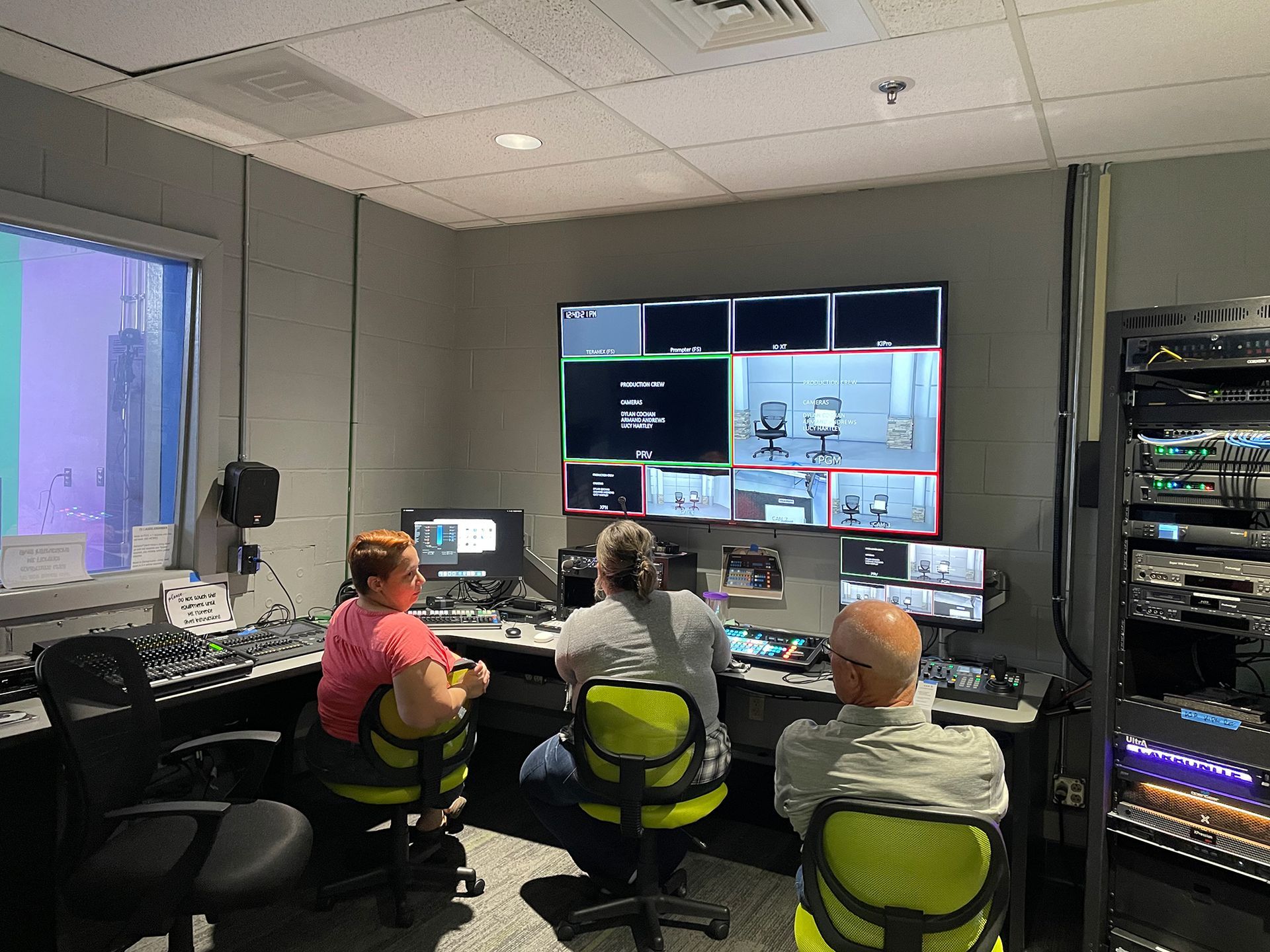 A group of people are sitting in front of a large screen in a control room.