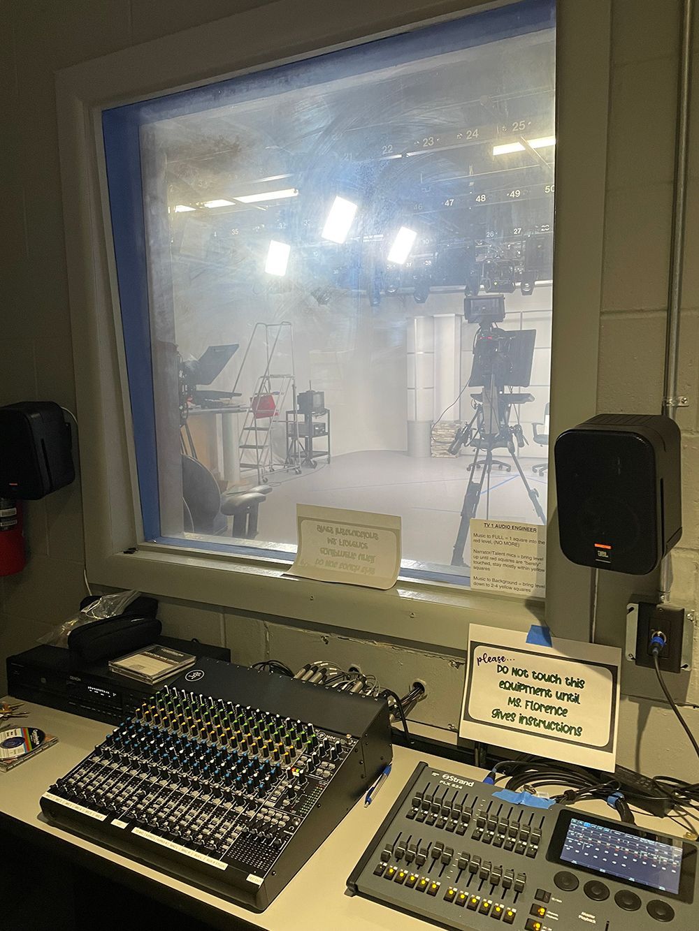 A mixer is sitting on a table in front of a window in a recording studio.