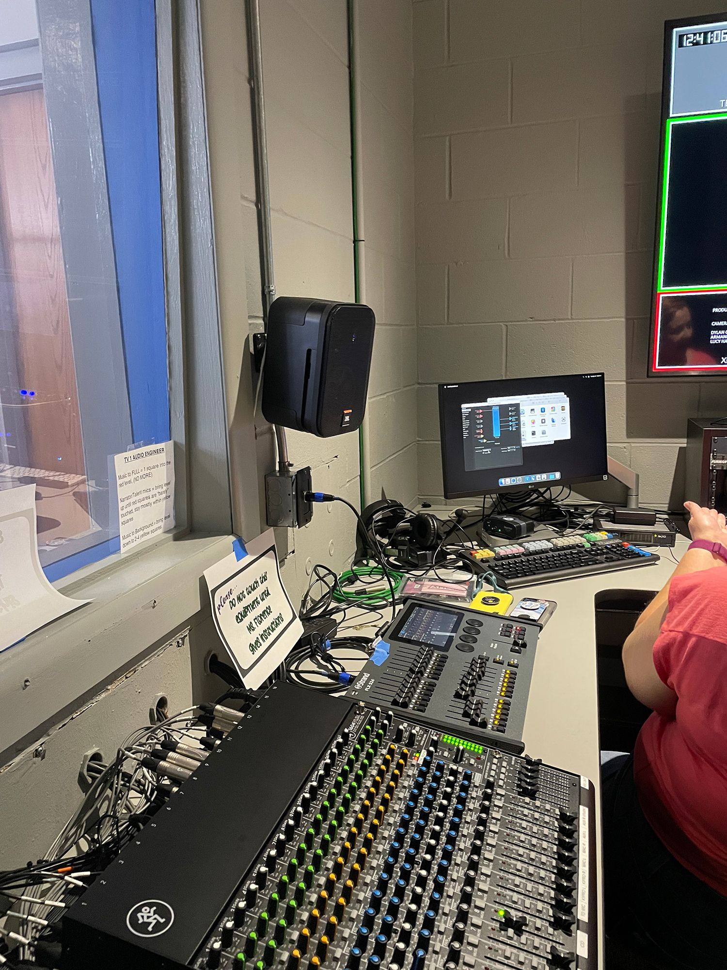A man is sitting at a desk in front of a mixer in a control room.