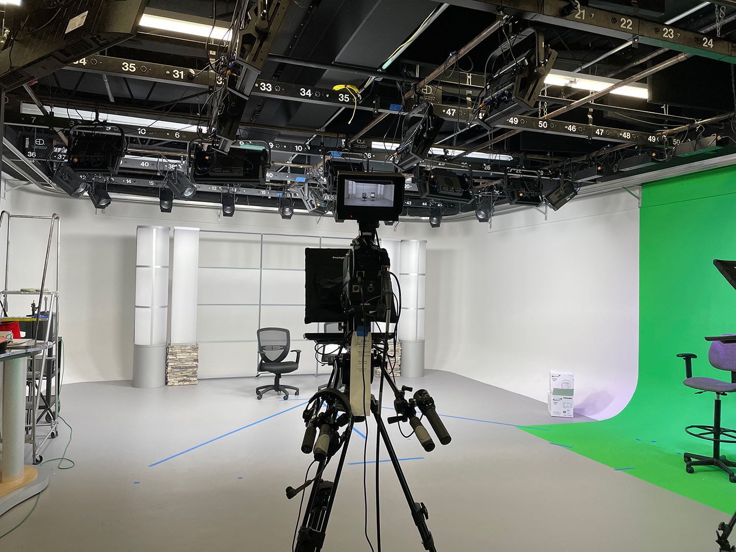 A camera is sitting on a tripod in a studio with a green screen.