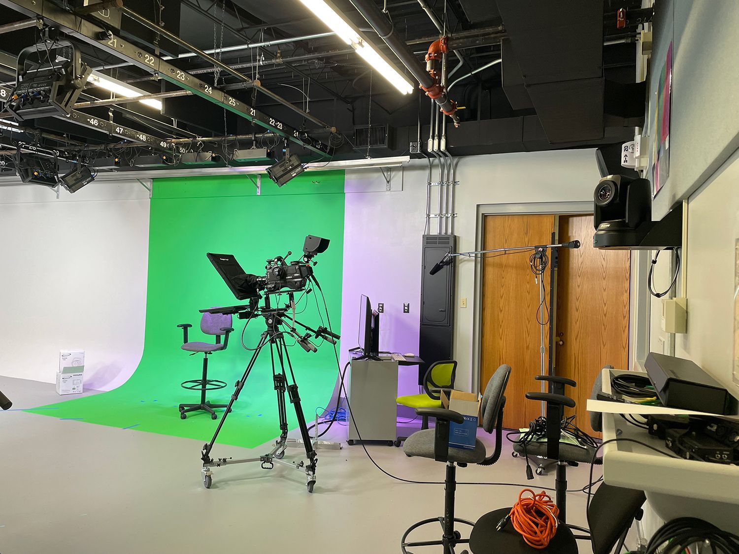 A video studio with a green screen and a camera on a tripod.