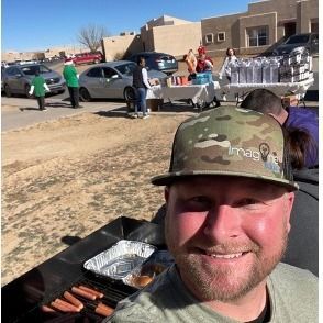 A man wearing a hat is standing in front of a grill.